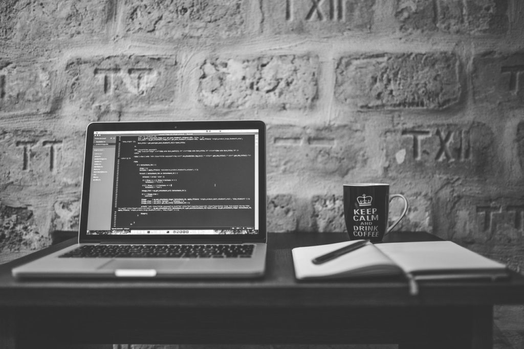 Laptop and notebook on desk.  Code on laptop screen.