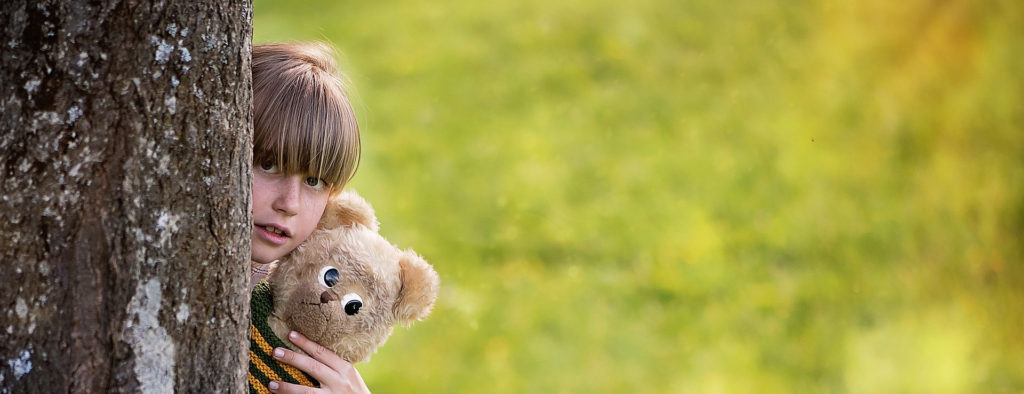 Girl hiding behind tree with teddy bear